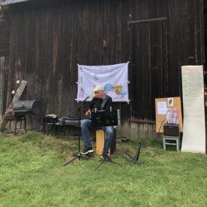 Ein Mann sitzt vor einer Scheune und macht Musik
