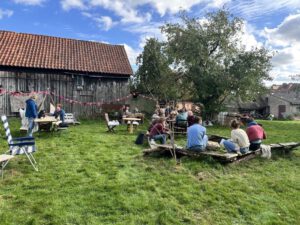 Menschen sitzen vor einer alten Scheune im Grünen