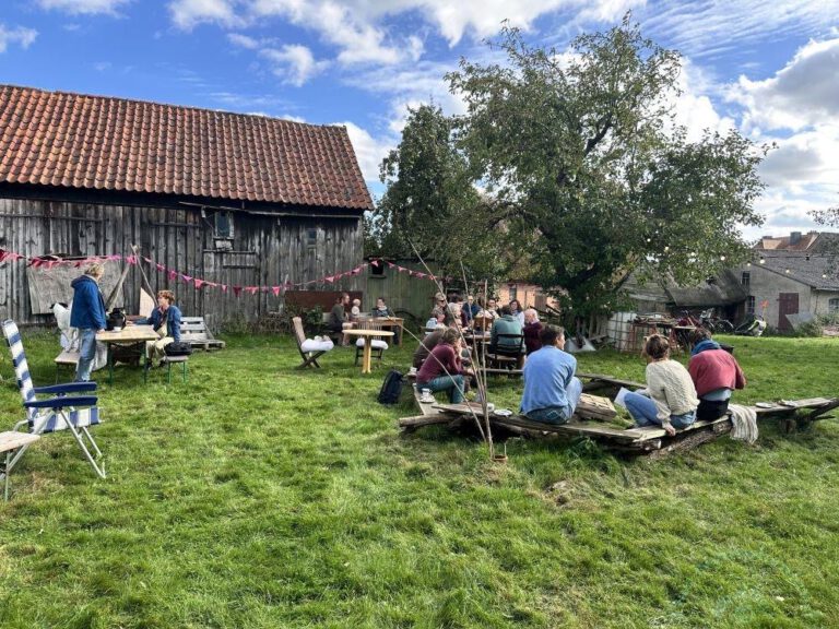 Menschen sitzen vor einer alten Scheune im Grünen