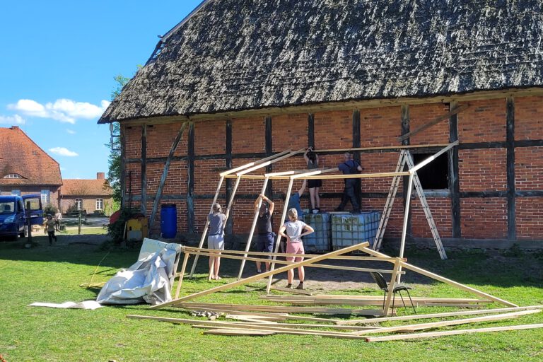 An einer alten Scheune wird ein Holzgerüst aufgebaut